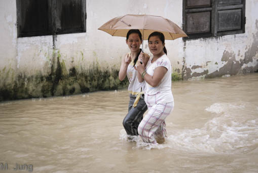 Zwei Mädchen mit Regenschriem laufen im knietiefen Hochwaser