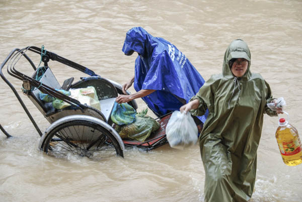 Rikscha steht im Hochwasser, zwei Personen entladen die Lebensmittel
