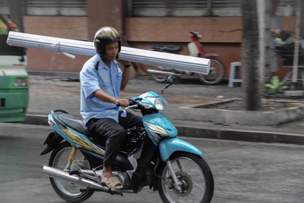 Mann transportiert eine große Jalousie auf der Schulter, Mann fährt auf einem Moped